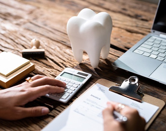 Large model tooth on desk next to laptop and hands working on invoice with calculator
