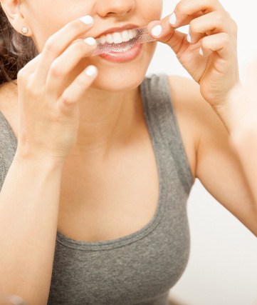 Woman putting on teeth whitening strip at home