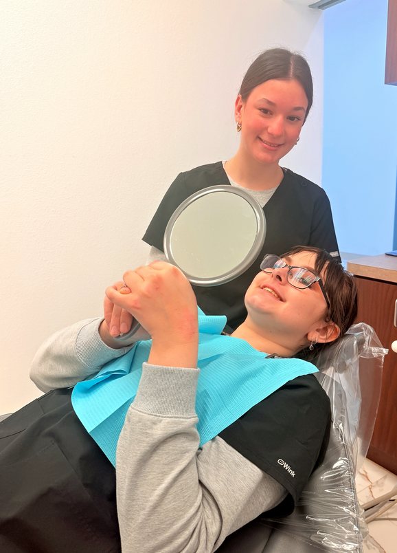 Smiling team member and a patient holding a hand mirror at Highland Oak Dental in Frisco